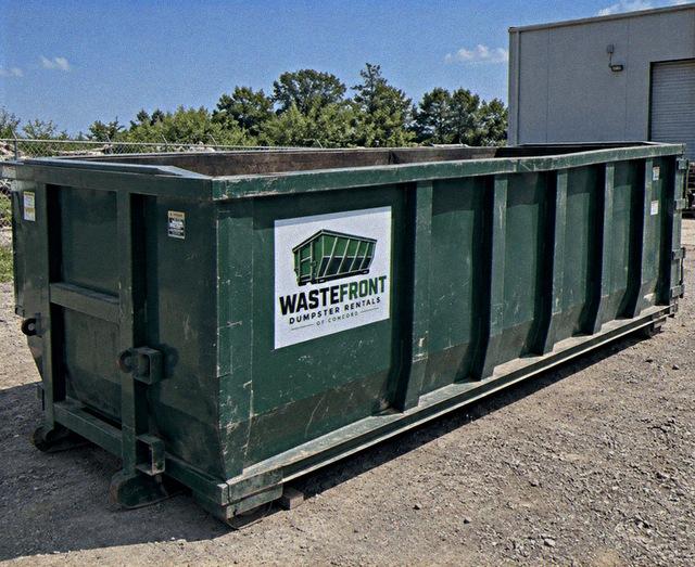 Green open-top container waiting on a gravel lot